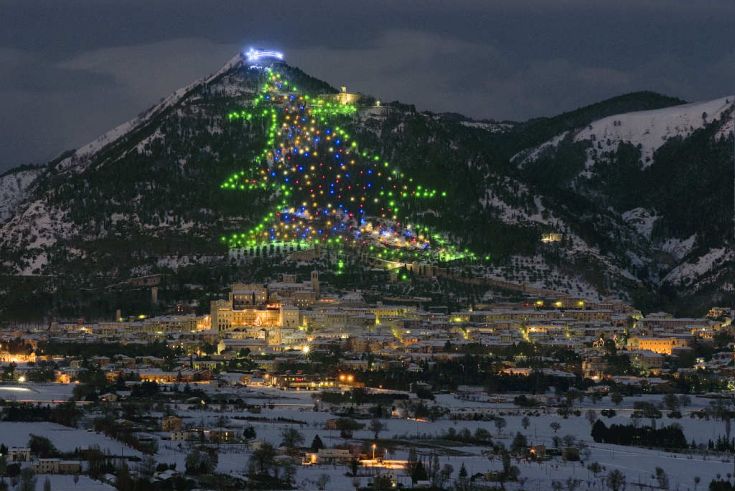 Un albero di Natale illuminato su una montagna innevata, con una vista sulla città sottostante.