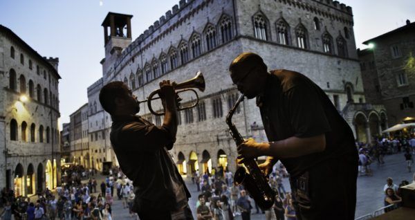 Due musicisti suonano dal vivo in piazza sotto il cielo serale, creando un'atmosfera vivace.