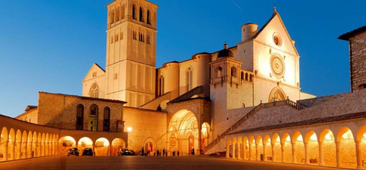 La Basilica di San Francesco a Assisi, illuminata di sera, mostra un'atmosfera tranquilla e suggestiva.