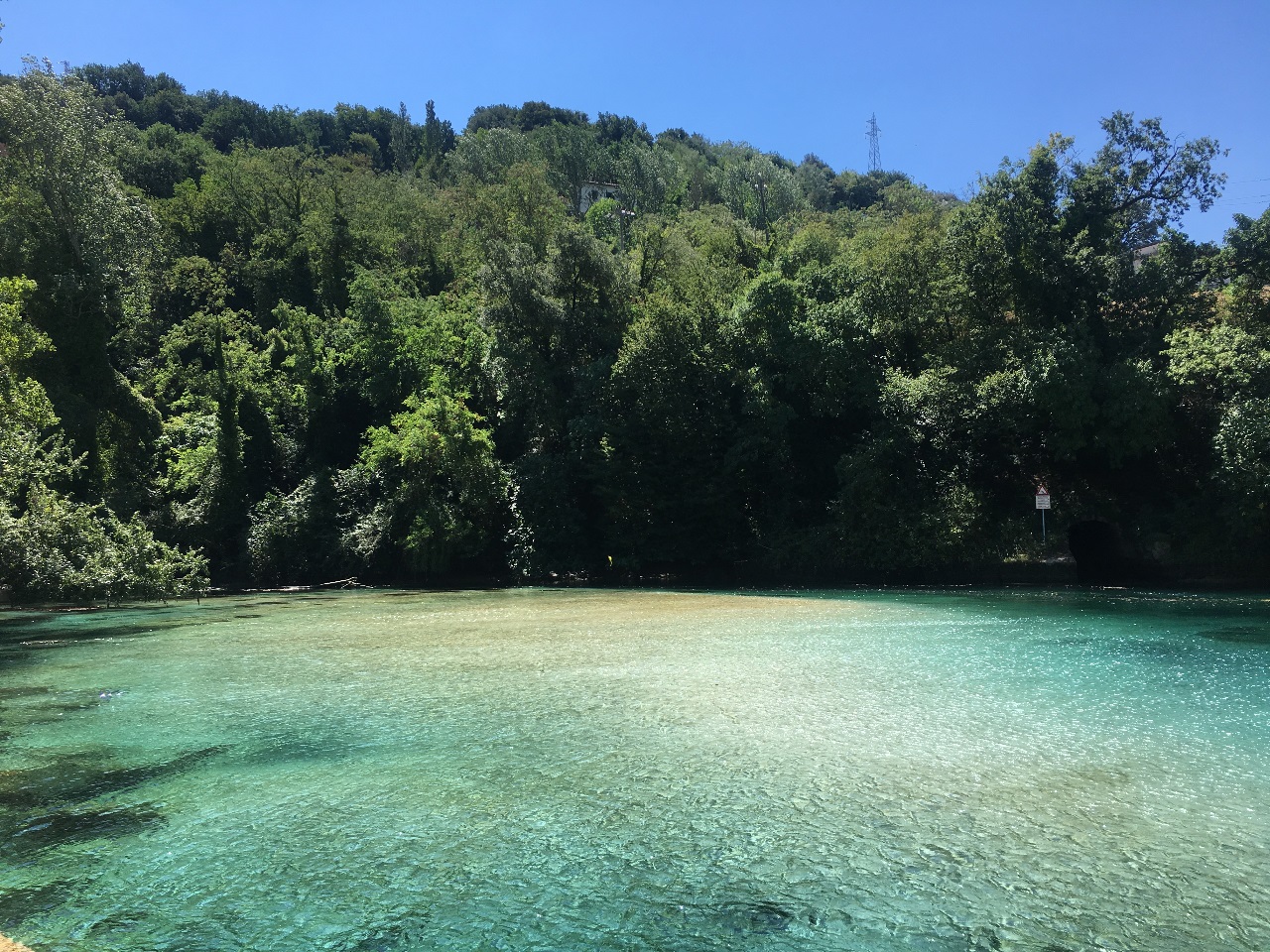 Un lago limpido circondato da vegetazione verdeggiante sotto un cielo sereno.