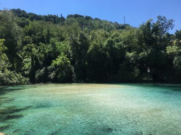 Un lago limpido circondato da vegetazione verdeggiante sotto un cielo sereno.