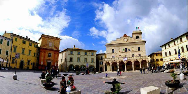 Scena di una piazza storica in Umbria con edifici colorati e persone che si godono attività all'aperto.