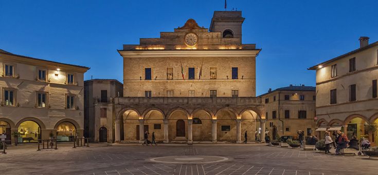 Piazza illuminata con la facciata storica del palazzo comunale, che crea un'atmosfera tranquilla al crepuscolo.