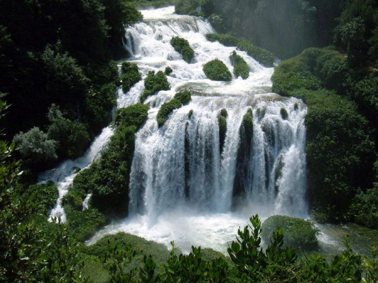 Un paesaggio naturale caratterizzato da una cascata che scorre attraverso una folta vegetazione.