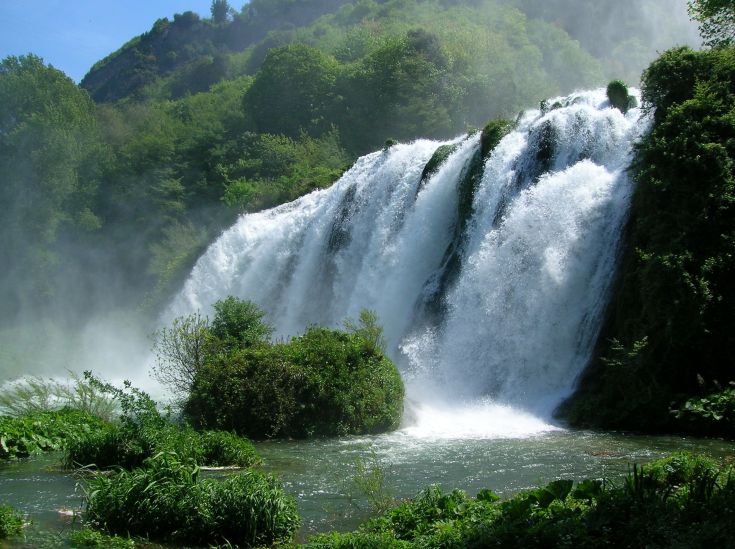 Una cascata immersa in un ambiente naturale, circondata da vegetazione e con acqua che fluisce.