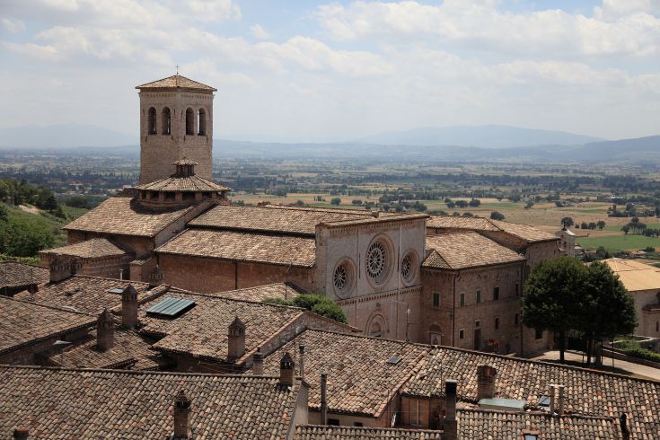 Vista di una chiesa ad Assisi e sullo sfondo la campagna umbra e le colline vicine. Un ambiente sereno e curato.