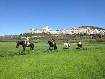 Un gruppo di cavalieri a cavallo si muove in un campo verde, con un antico palazzo in lontananza.