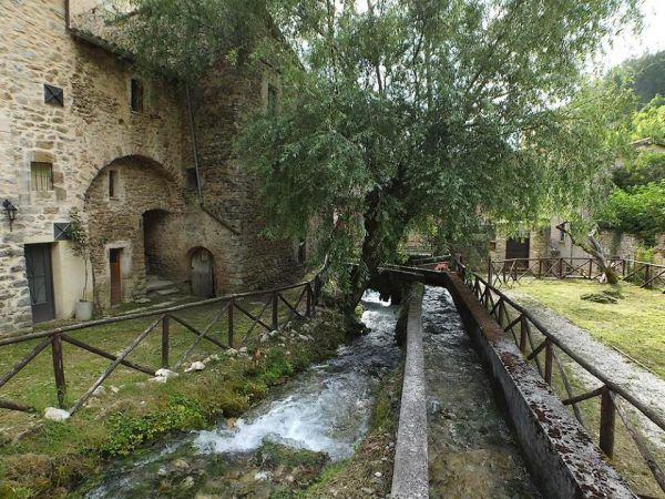 Un tranquillo villaggio circondato dalla natura, con un ruscello che scorre dolcemente accanto a un palazzo in pietra.