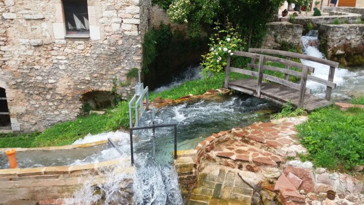 Un corso d'acqua tranquillo scorre attraverso una zona verde con un ponte in legno.