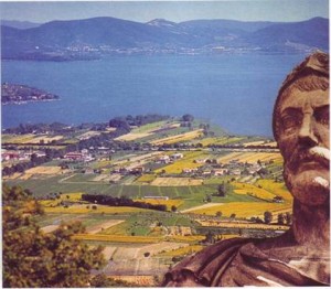 Una statua si erge sul paesaggio lacustre a simboleggiare la battaglia di Annibale, con un lago blu visibile in lontananza.