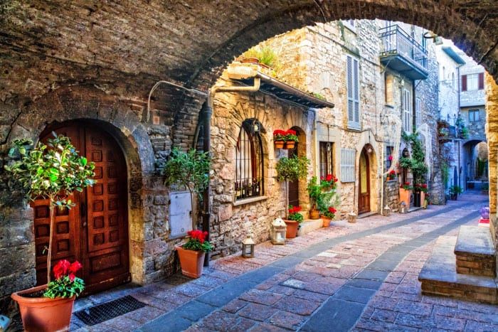 Un tipico vicolo in pietra in Umbria, decorato con piante fiorite e con un’atmosfera storica.