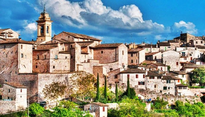 Un borgo umbro caratterizzato da costruzioni in pietra e un campanile che si eleva sotto un cielo sereno.