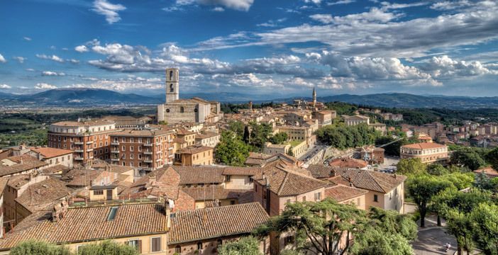 Panorama su una città umbra, circondata da colline verdi e un cielo sereno.