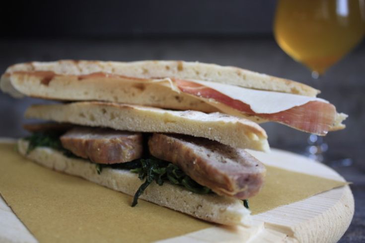 Un panino gourmet con carne e verdure fresche, presentato su un piatto di legno.