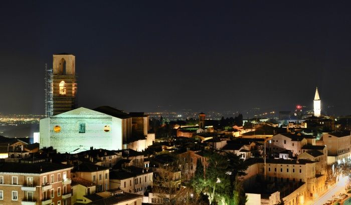 Panorama notturno di una città storica con palazzi illuminati e torri, che mostra l'eleganza dell'architettura tradizionale.