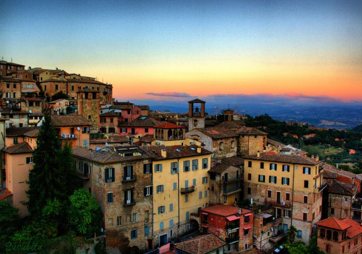 Panorama di un antico borgo al tramonto, con colori caldi nel cielo e edifici storici ben visibili.