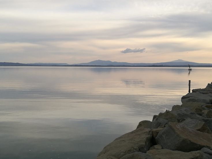 Un tranquillo paesaggio lacustre al tramonto, con colline in lontananza.