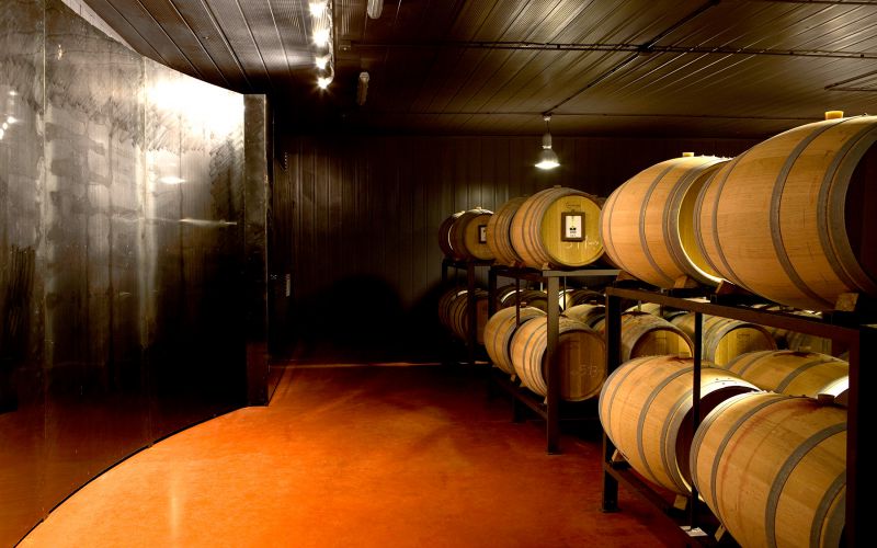 Interno di una cantina, dotato di botti di legno, illuminato da luci soffuse che creano un'atmosfera accogliente.