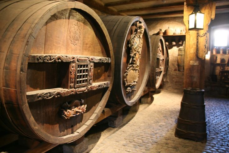 Interno di un palazzo con grandi botti di legno, elementi decorativi e pavimento in pietra.