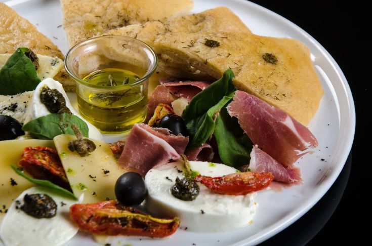 Un piatto assortito con affettati e formaggi, servito insieme a fette di pane e un filo d'olio d'oliva.