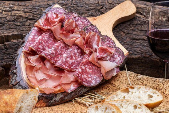 Un tagliere di salumi con assortimento di carni e pane fresco, accompagnato da un bicchiere di vino rosso.