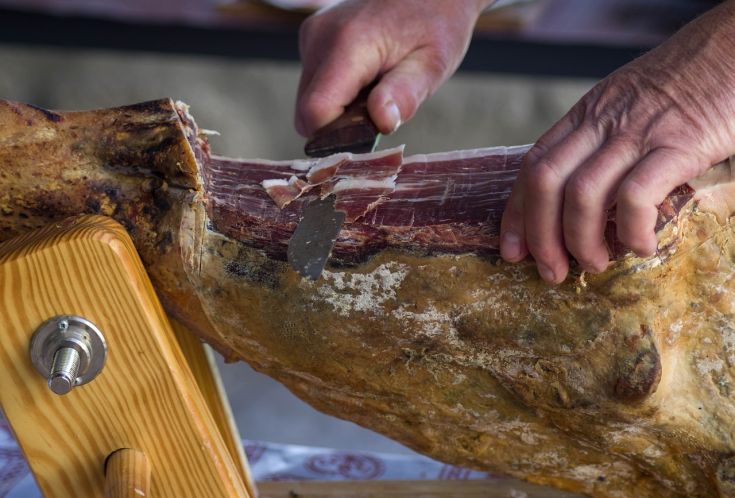 Un professionista affetta con attenzione un prosciutto, evidenziando la tecnica dell'arte norcina.