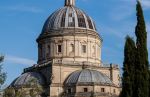 Cupola di Santa Maria della Consolazione a Todi, circondata da cipressi e cielo sereno.
