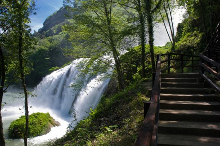 Una cascata immersa nel verde, circondata da vegetazione rigogliosa, con scale che portano a una vista panoramica.