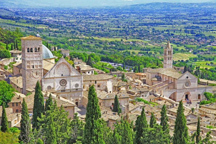 Scena di Assisi caratterizzata da architettura storica e un paesaggio naturale.