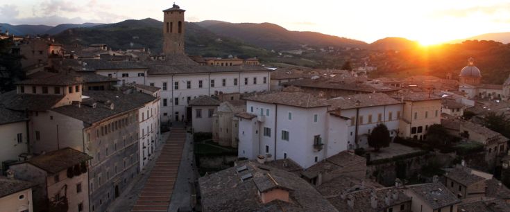 Tramonto su una cittadina storica, tra tetti in pietra e colline sullo sfondo.