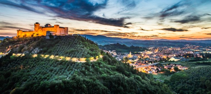 Rocca di Spoleto illuminata al tramonto, circondato da colline e vigneti tipici della campagna umbra.