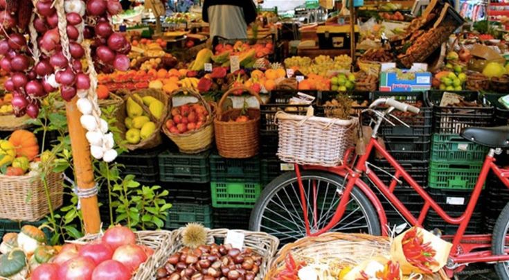 Un mercato vivace e colorato con una varietà di frutta e verdura fresca. Una bicicletta rossa si distingue tra le bancarelle.