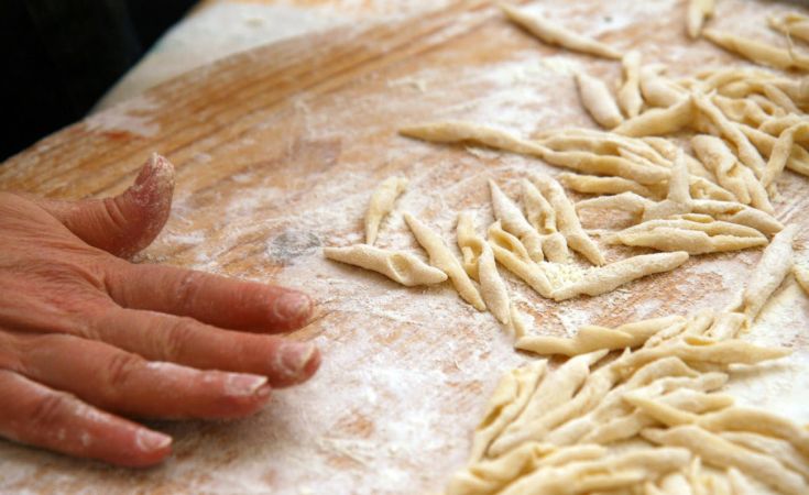 Una mano che sta lavorando la pasta fresca tradizionale su un tavolo cosparso di farina.