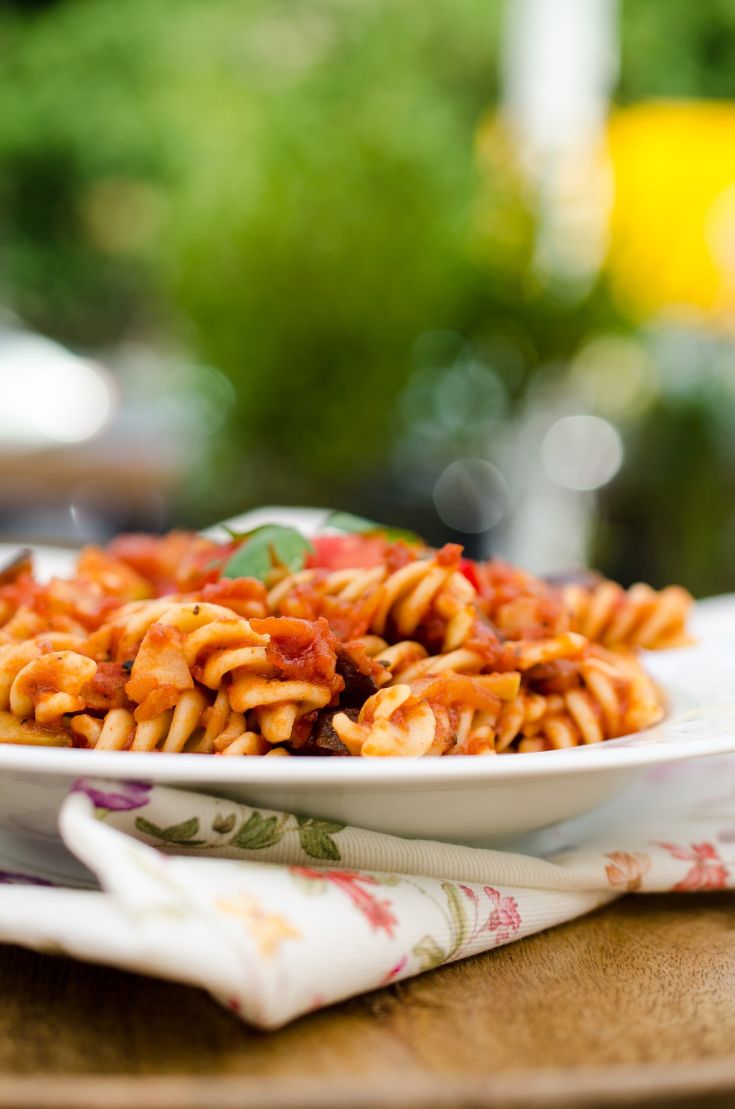 Un piatto di pasta con salsa di pomodoro, arricchita da pomodori freschi e spezie, servita all'esterno.