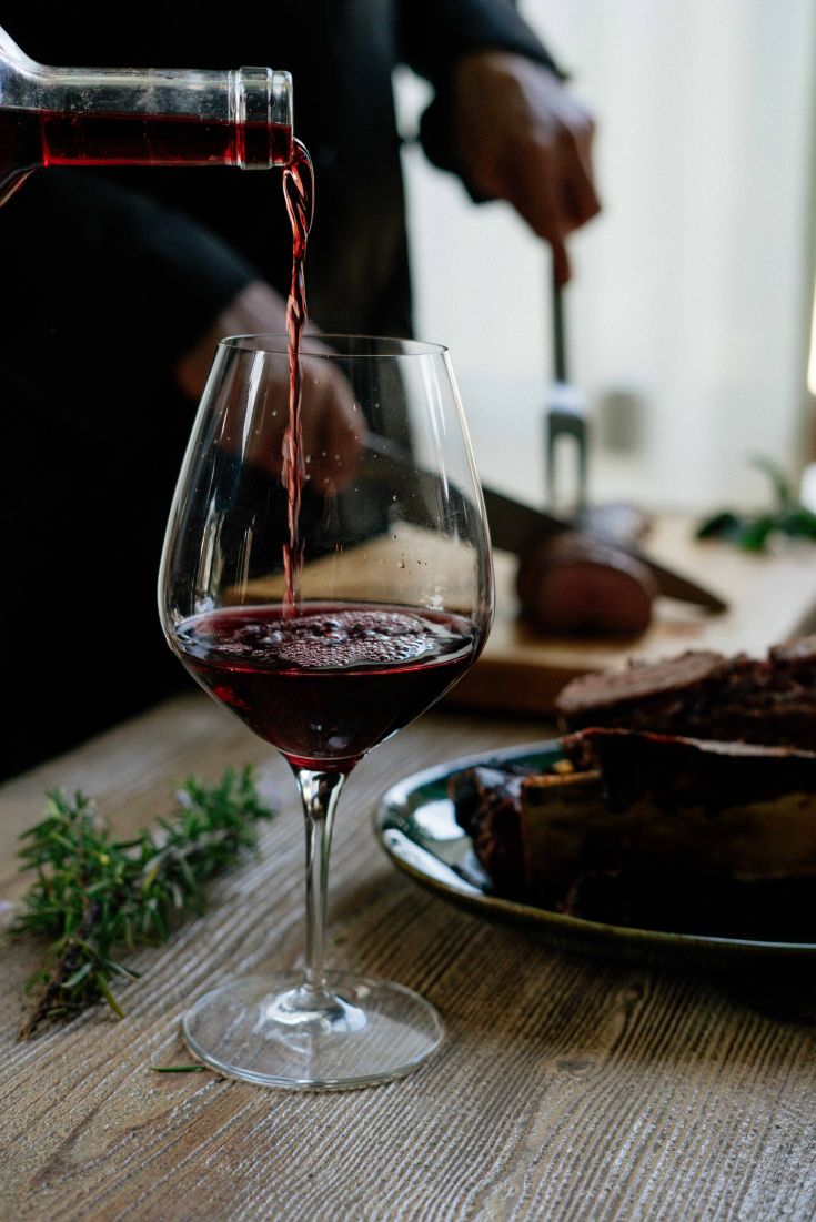 Un bicchiere di vino rosso viene versato, con piatti appetitosi in evidenza nella cucina.