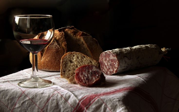 Un bicchiere di vino rosso, pane fresco e salumi su un tavolo di legno.