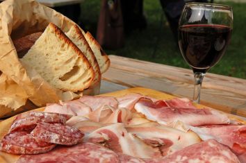 Un semplice tagliere di salumi assortiti, accompagnato da pane e vino rosso, ottimo per un picnic all'aperto.