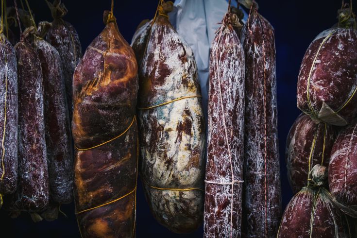Diversità di salumi appesi in mostra, pronti per essere assaporati.