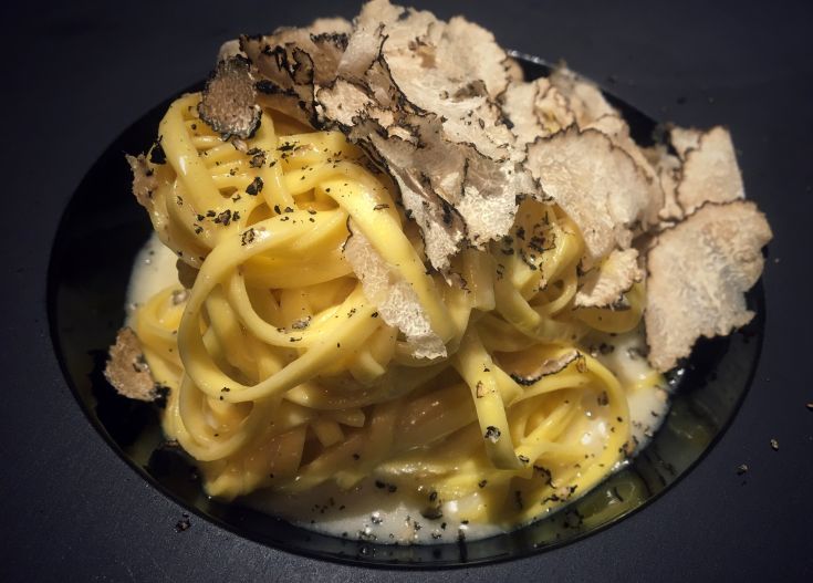 Piatto di pasta cremosa, decorato con fette di tartufo bianco.