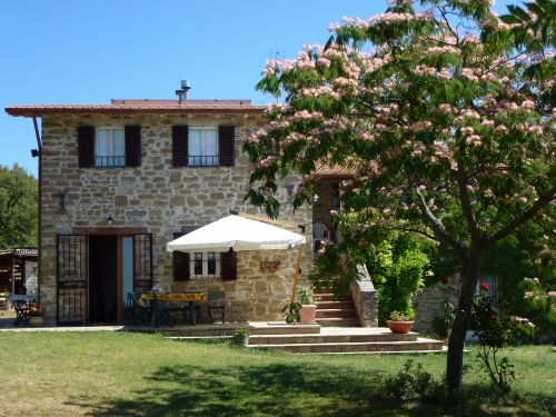 Casale in pietra circondato da un ampio giardino con varie piante e fiori, situato in un'area verde e tranquilla.