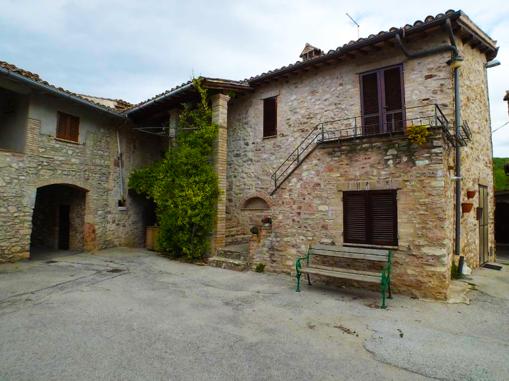 Un angolo di un tranquillo di un casolare con pietre a vista e una panchina verde nel suo contesto esterno.