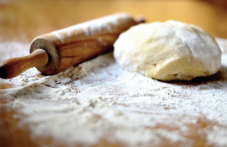 Un panetto di pasta fresca, mattarello e farina sopra una spianatoia, gli ingredienti per la preparazione della pasta fresca fatta in casa.