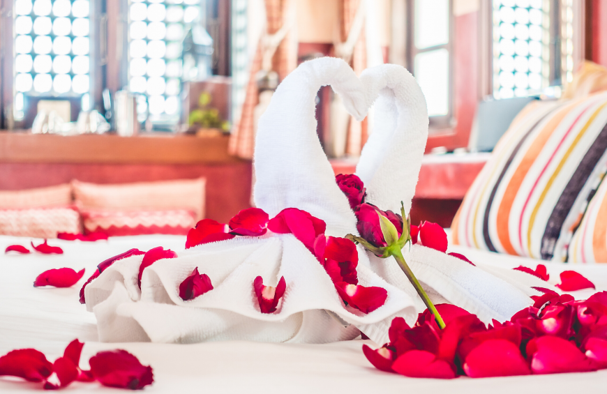 Una scultura di asciugamani a forma di cigno  disposta sopra un letto, circondata da petali di rosa.