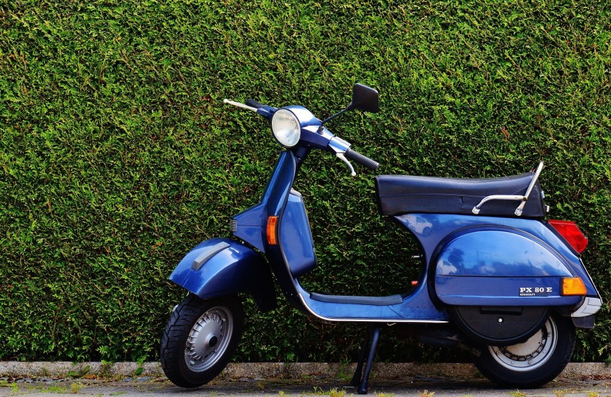 Una vespa blu parcheggiata davanti ad una siepe, evocando un senso di libertà.