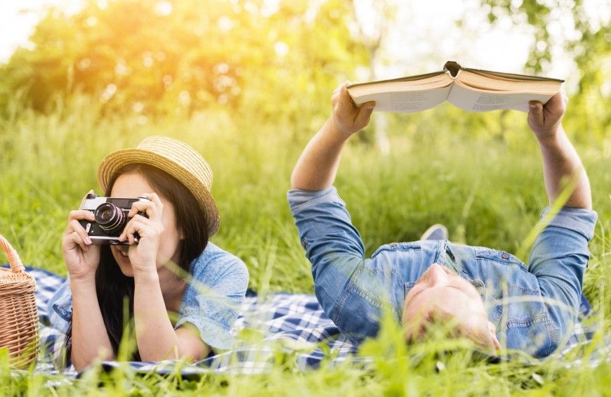 Una coppia trascorre una giornata tranquilla all'aperto, lei con una macchina fotografica e lui intento nella lettura di un libro.