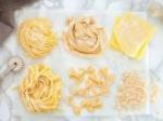 Diverse varietà di pasta fatta a mano disposte su un piano di lavoro. Le forme e i colori variati offrono un aspetto invitante.