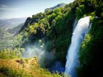 Scena di una cascata immersa in un ambiente naturale, circondata da vegetazione verde.