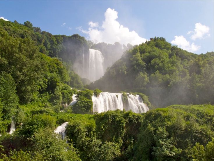 Una scena della cascata delle Marmore, con acqua chiara circondate da vegetazione verde.