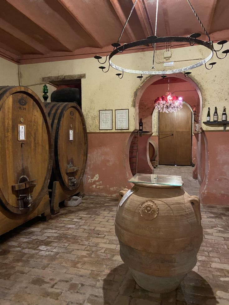 Interno di un palazzo con botti in legno e un'antica anfora. Atmosfera sobria e tradizionale.