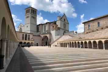 Scena della Basilica di San Francesco a Assisi, circondata da edifici storici e atmosfera tranquilla.